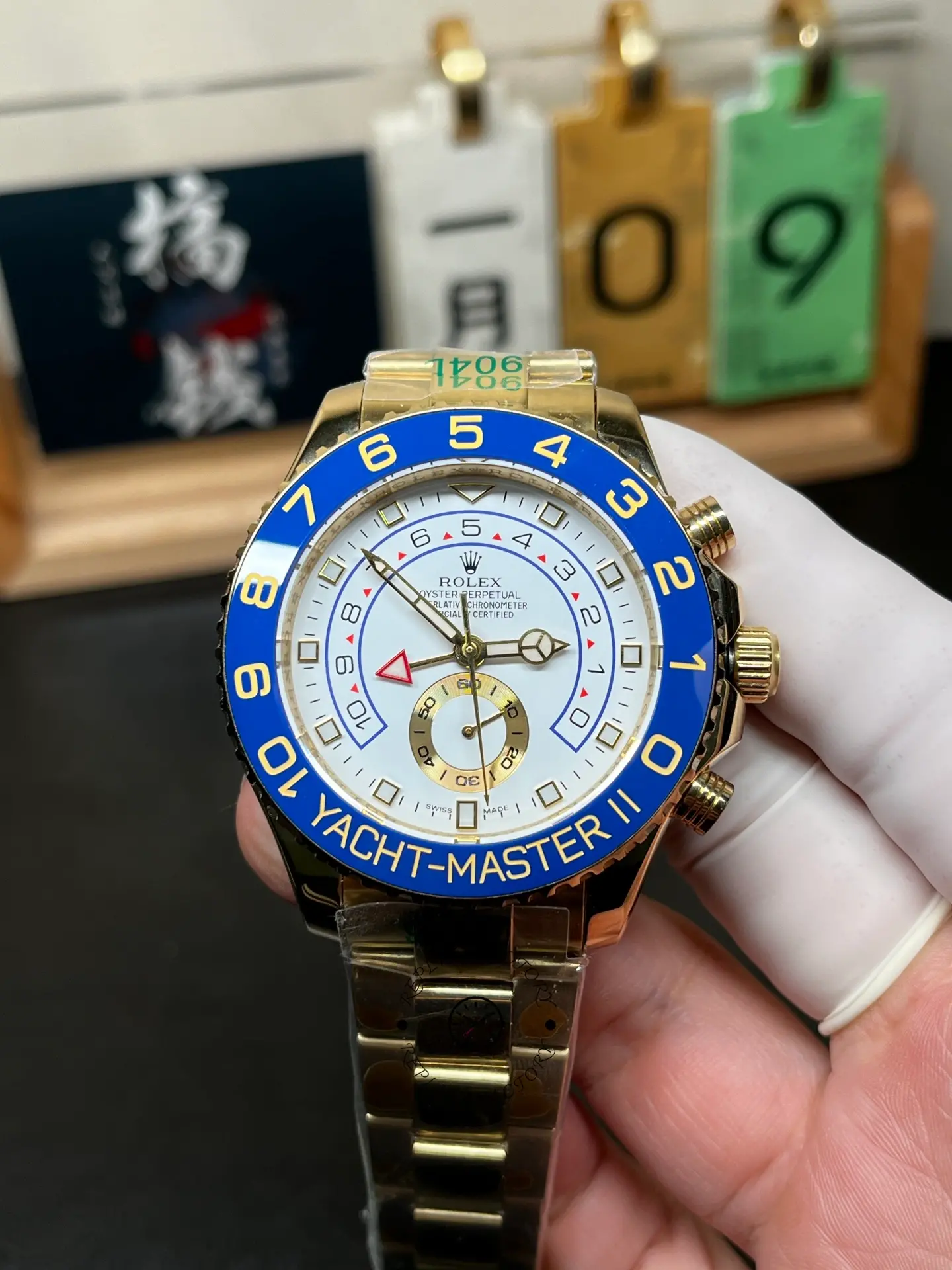 Front view of Rolex Yacht-Master II 116688 with white dial, blue bezel and gold-tone bracelet held in hand.