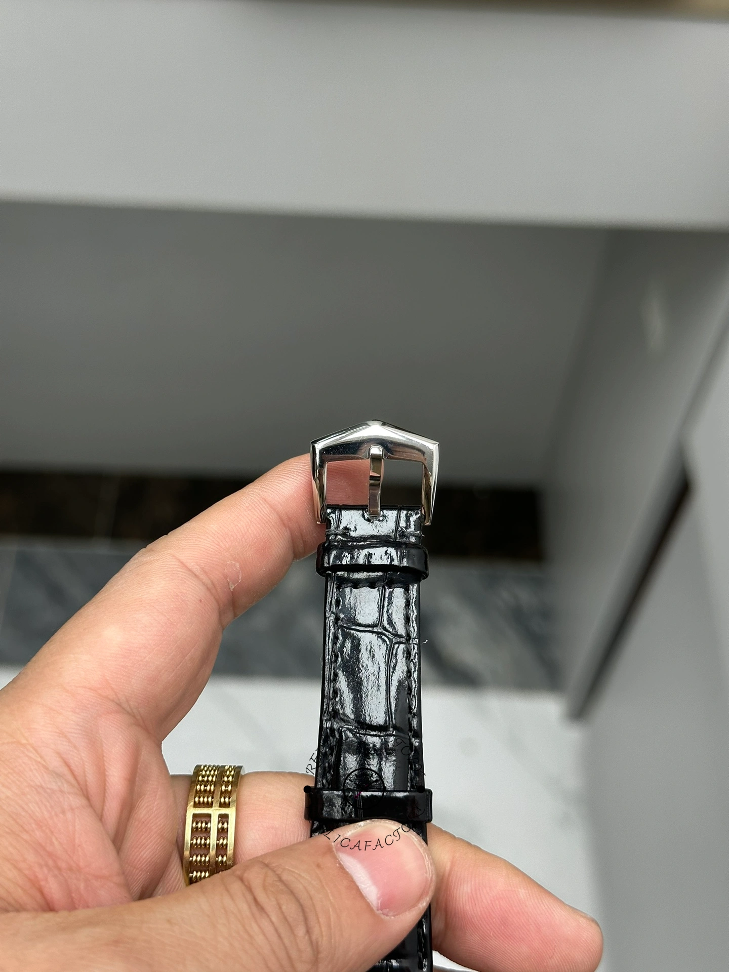 Strap buckle detail of Patek Philippe Calatrava 6119G-001 showing clasp end and black leather texture.