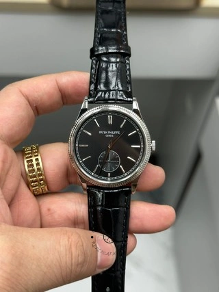 Hand-held front view of Patek Philippe Calatrava 6119G-001 showing black dial and leather strap.