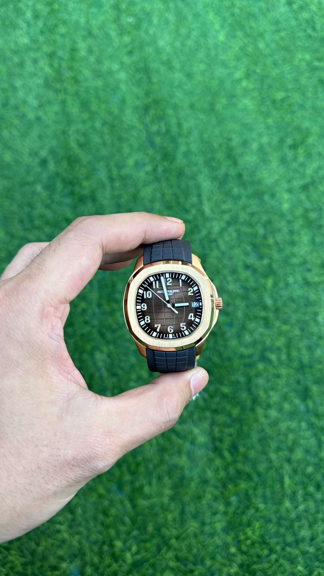 Hand-held front view of Patek Philippe Aquanaut 5167R-001 highlighting luminous numerals and minute track.