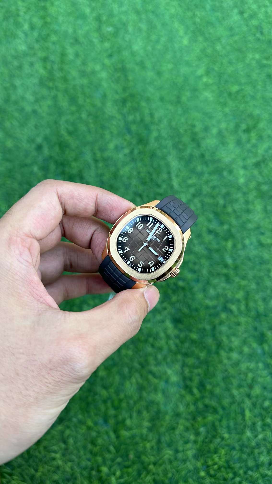 Hand-held angle of Patek Philippe Aquanaut 5167R-001 showing embossed dial pattern and polished case edge.