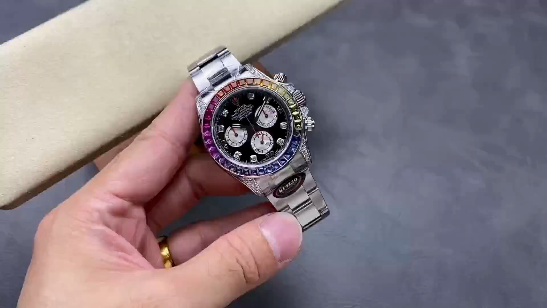 Handheld view of the Rolex Daytona 116599RBOW showing the black dial and rainbow sapphire bezel. - Video