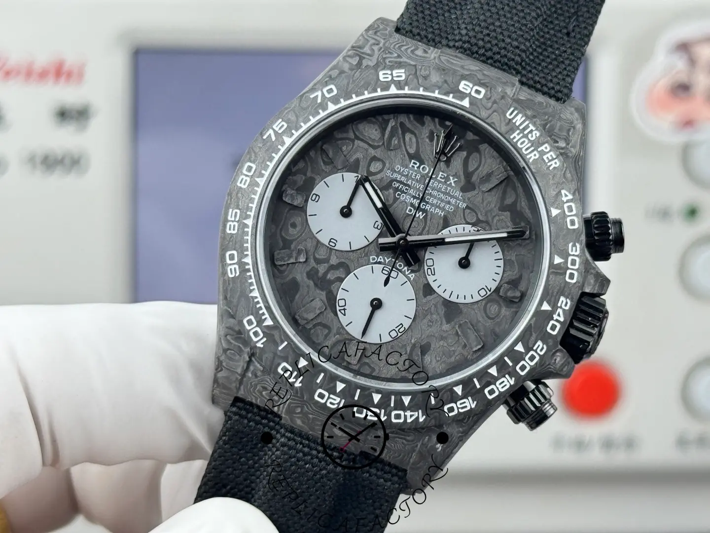 Replica Rolex DiW Daytona All Carbon Graphite 40mm, full watch held in hand against testing machine background.