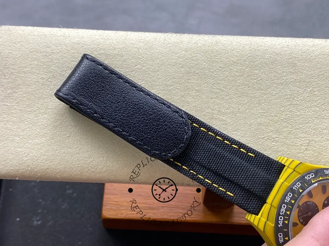 Rolex Daytona DIW, strap close-up showing black leather texture and yellow stitching along the edge.