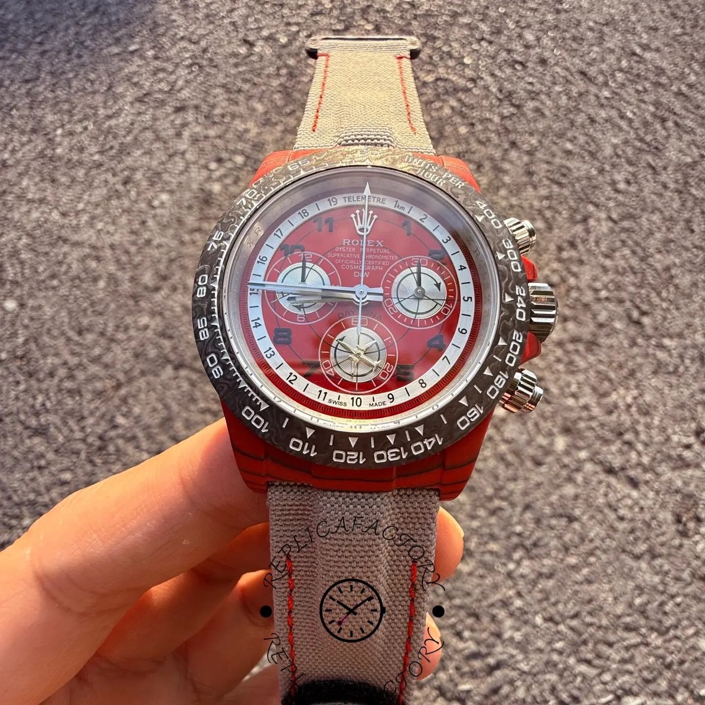 Front view of the Rolex Daytona DiW carbon case with red dial, black tachymeter bezel and grey fabric strap.